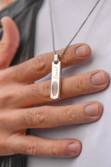 Close up of men's silver engraved bar necklace held in hand stainless steel