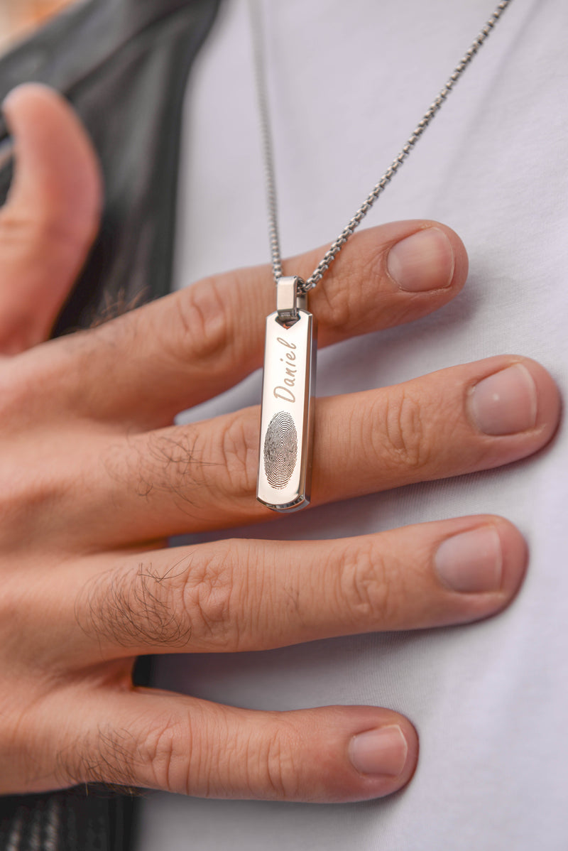 Close up of men's silver engraved bar necklace held in hand stainless steel