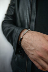 Men's silver and black bead bracelet worn on wrist dark background stainless steel